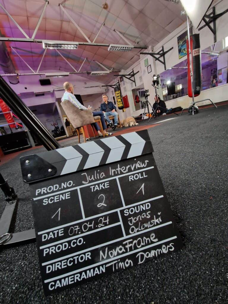 Eine Filmklappe lehnt an einem Stativ in mitten eines Filmsets